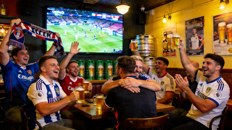一群球迷在酒吧通过大屏幕观看高清英超足球直播的欢乐场景